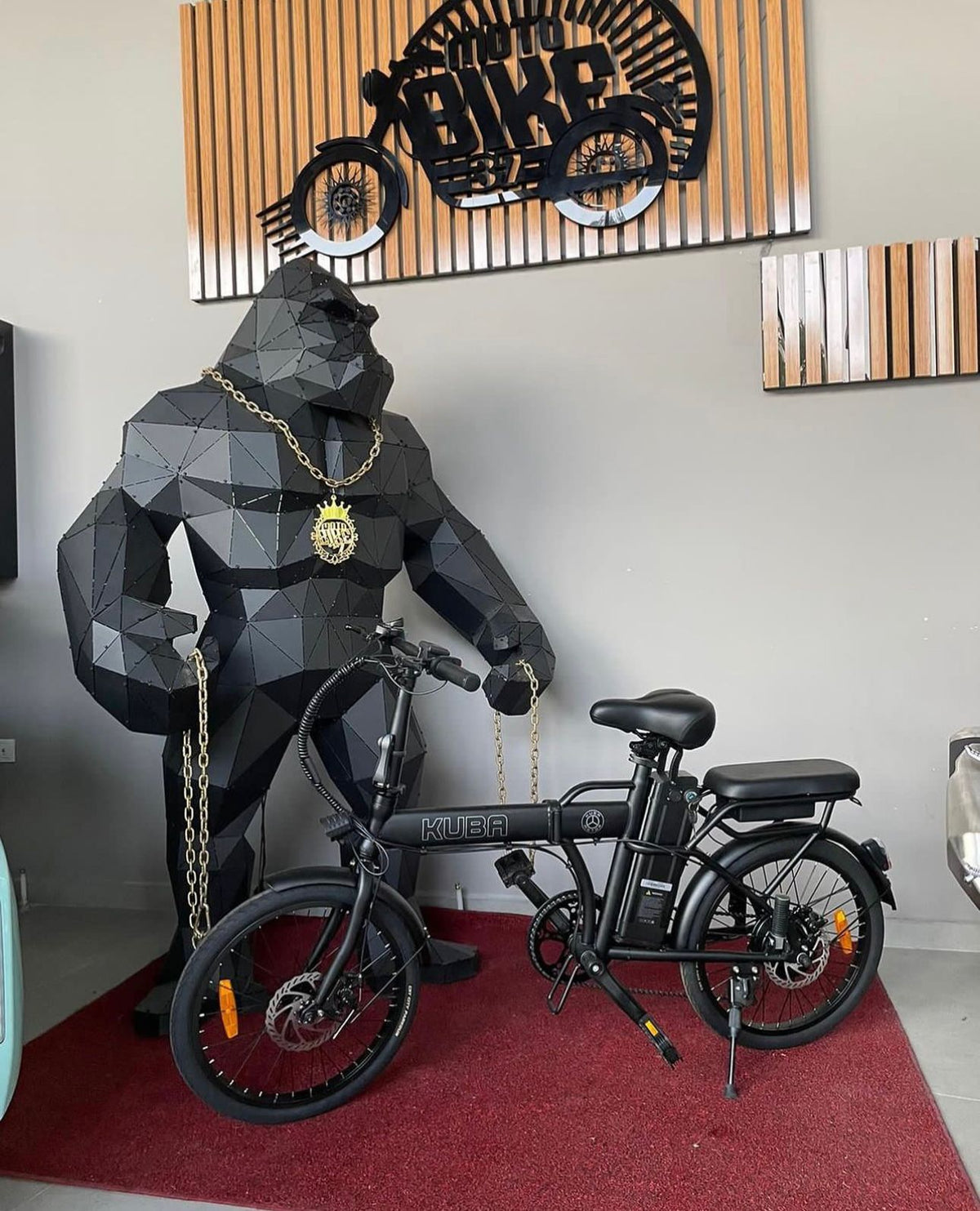 Large geometric black gorilla sculpture with gold chain next to a black KUBA electric bike.
