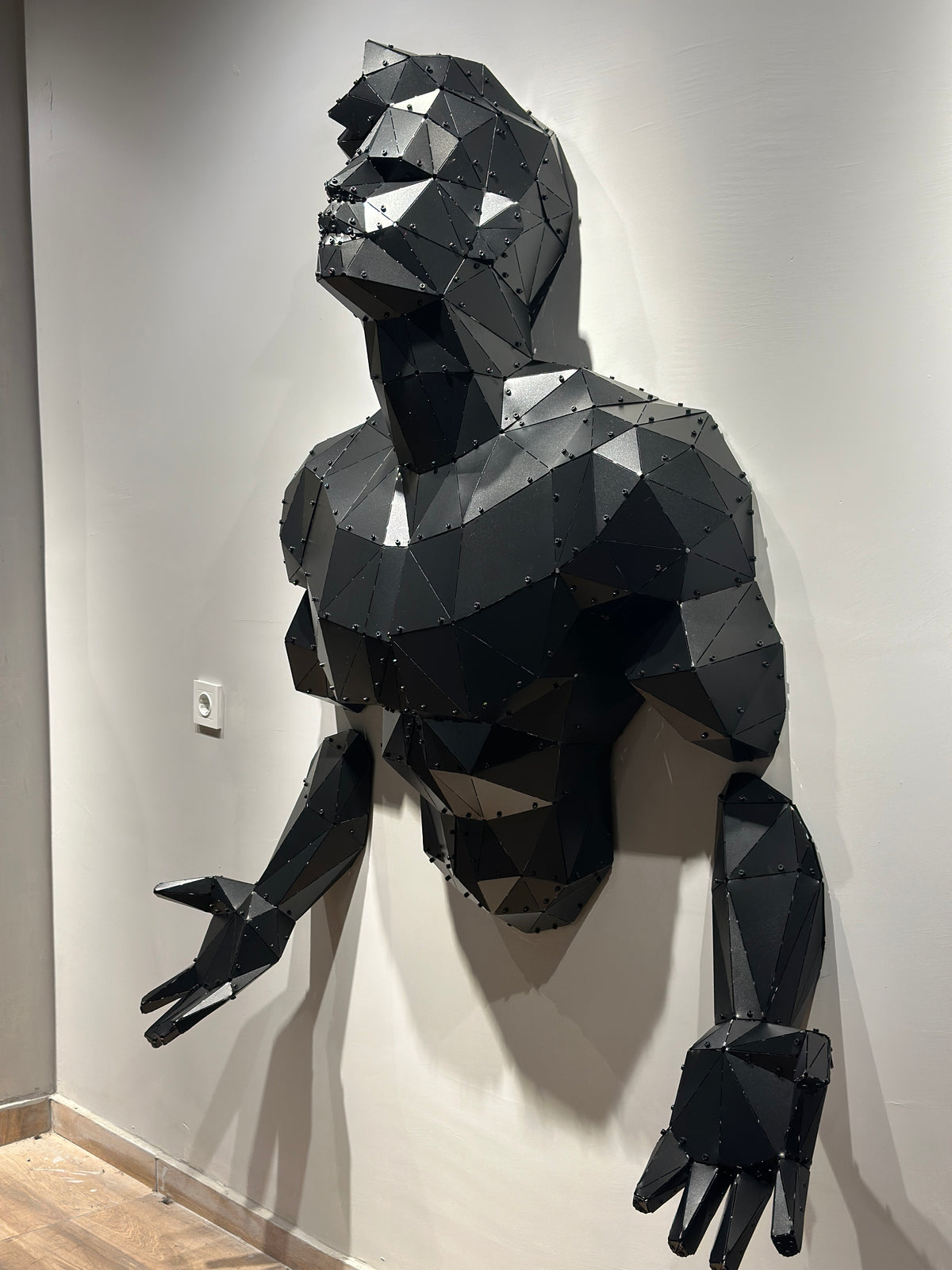Large geometric black metal bodybuilder torso wall sculpture emerging from a white wall