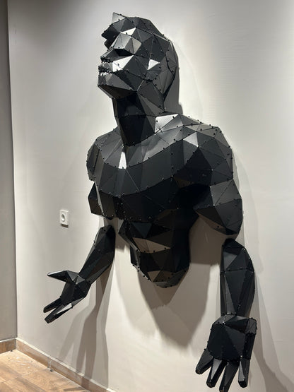 Large geometric black metal bodybuilder torso wall sculpture emerging from a white wall