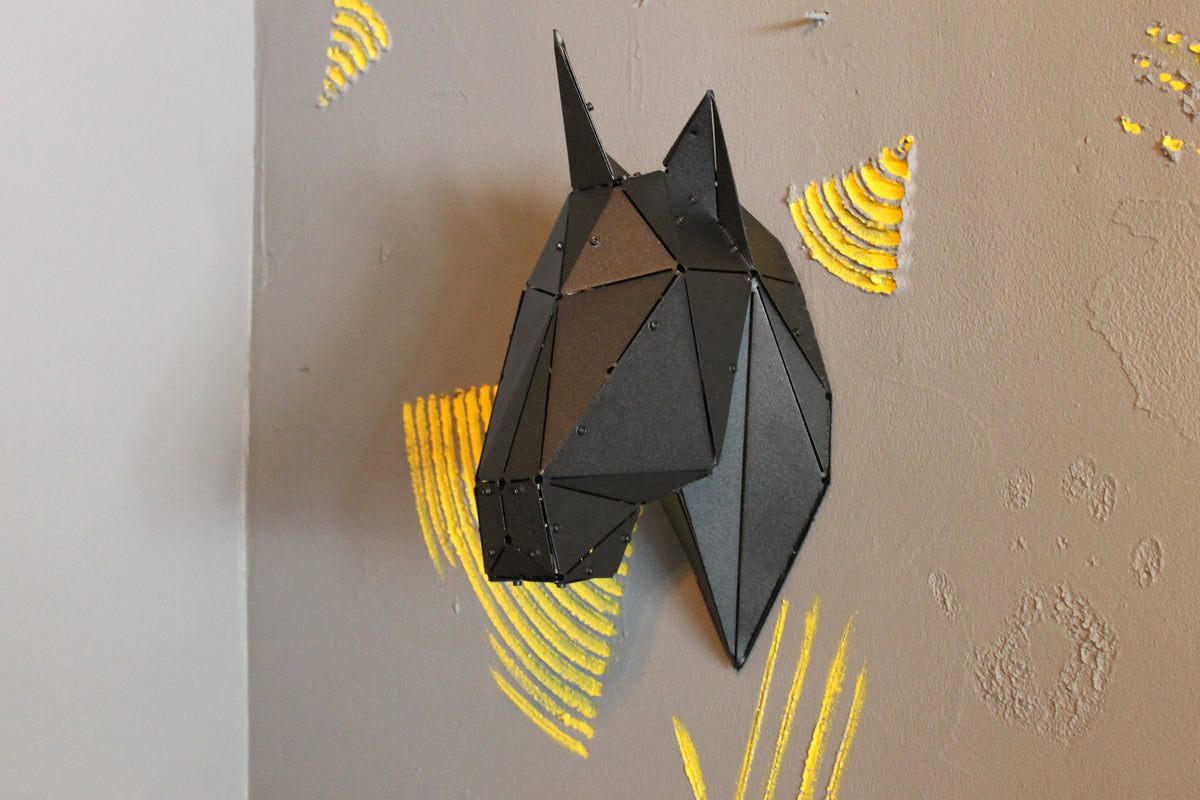Low-poly black metal horse head sculpture mounted on a grey wall with yellow accents.