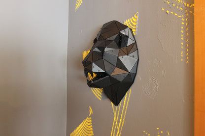 Low-poly black metal lion head wall sculpture on a grey wall with yellow accents