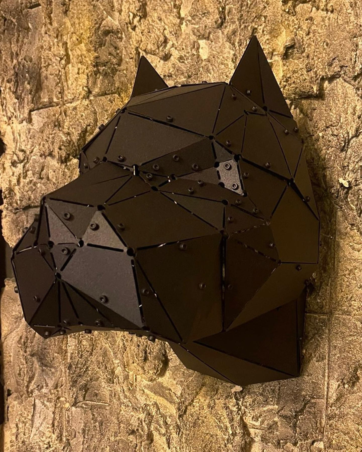 Low-poly black metal pitbull head sculpture mounted on a textured stone wall