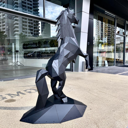 Low-poly black metal rearing horse sculpture on a round base in front of a glass storefront