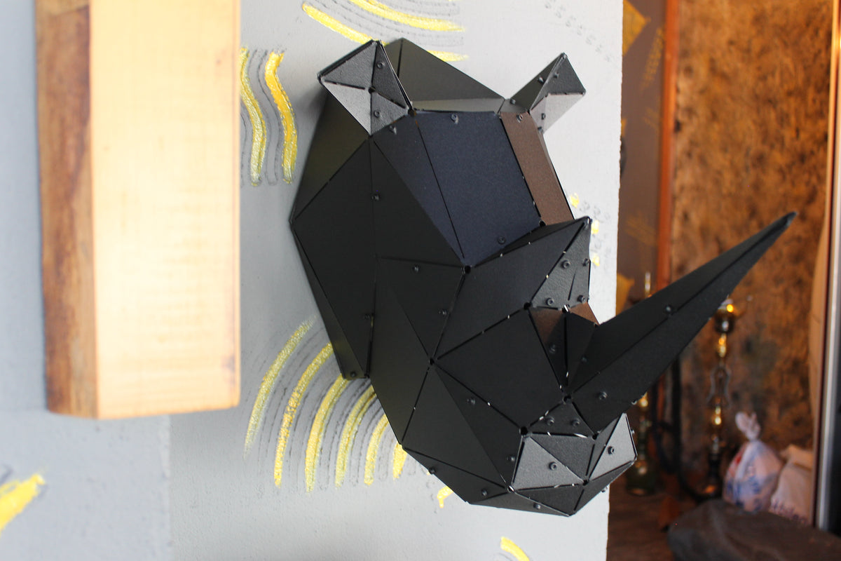 Low-poly black metal rhinoceros head sculpture mounted on a light gray wall