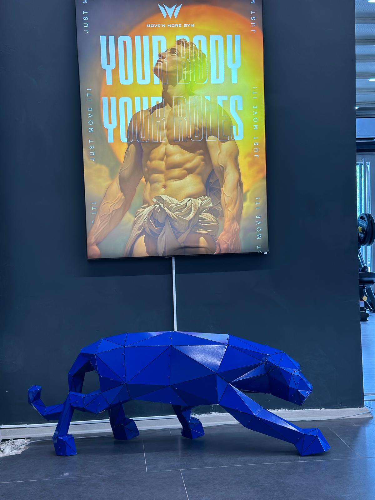 Low-poly blue metal panther sculpture in front of a fitness gym poster