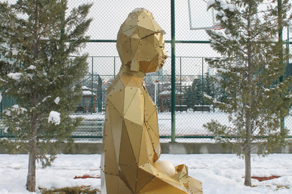 Side profile of low-poly gold metal Buddha sculpture seated in snow