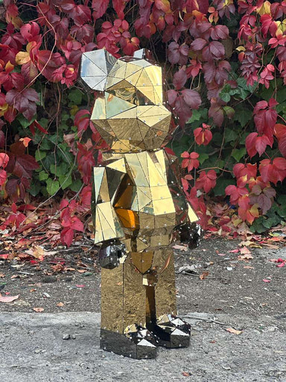 Low-poly gold metallic bear sculpture standing against red autumn leaves