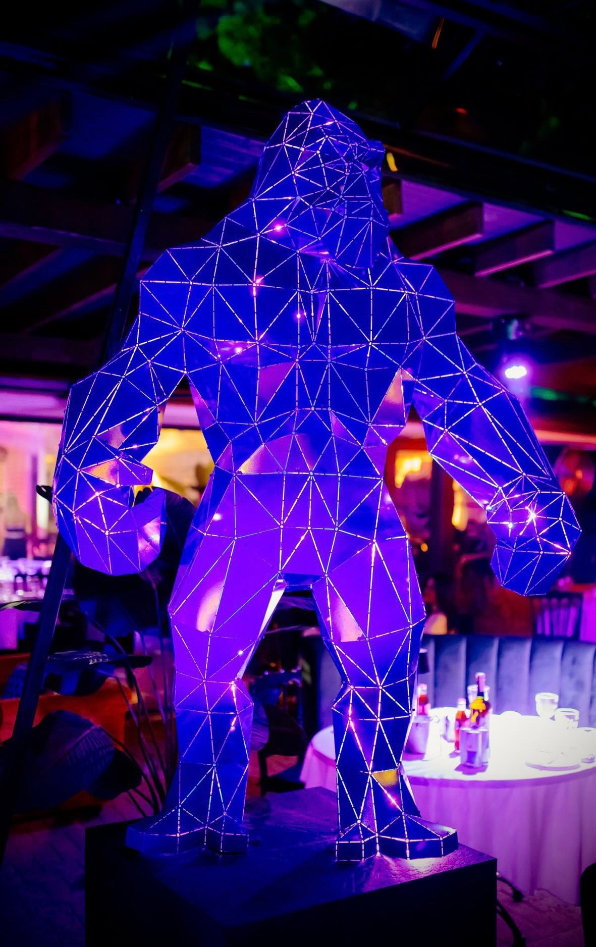 Low-poly geometric gorilla sculpture illuminated with purple neon lights in a luxury interior.