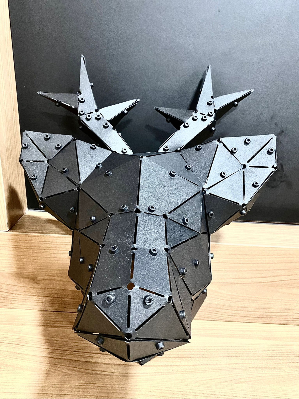 Low-poly handcrafted black metal deer head sculpture on a wooden surface