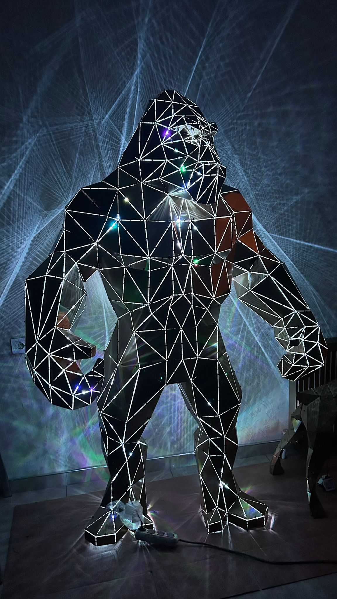 Low-poly handcrafted metal gorilla sculpture with integrated LED lighting against a laser backdrop