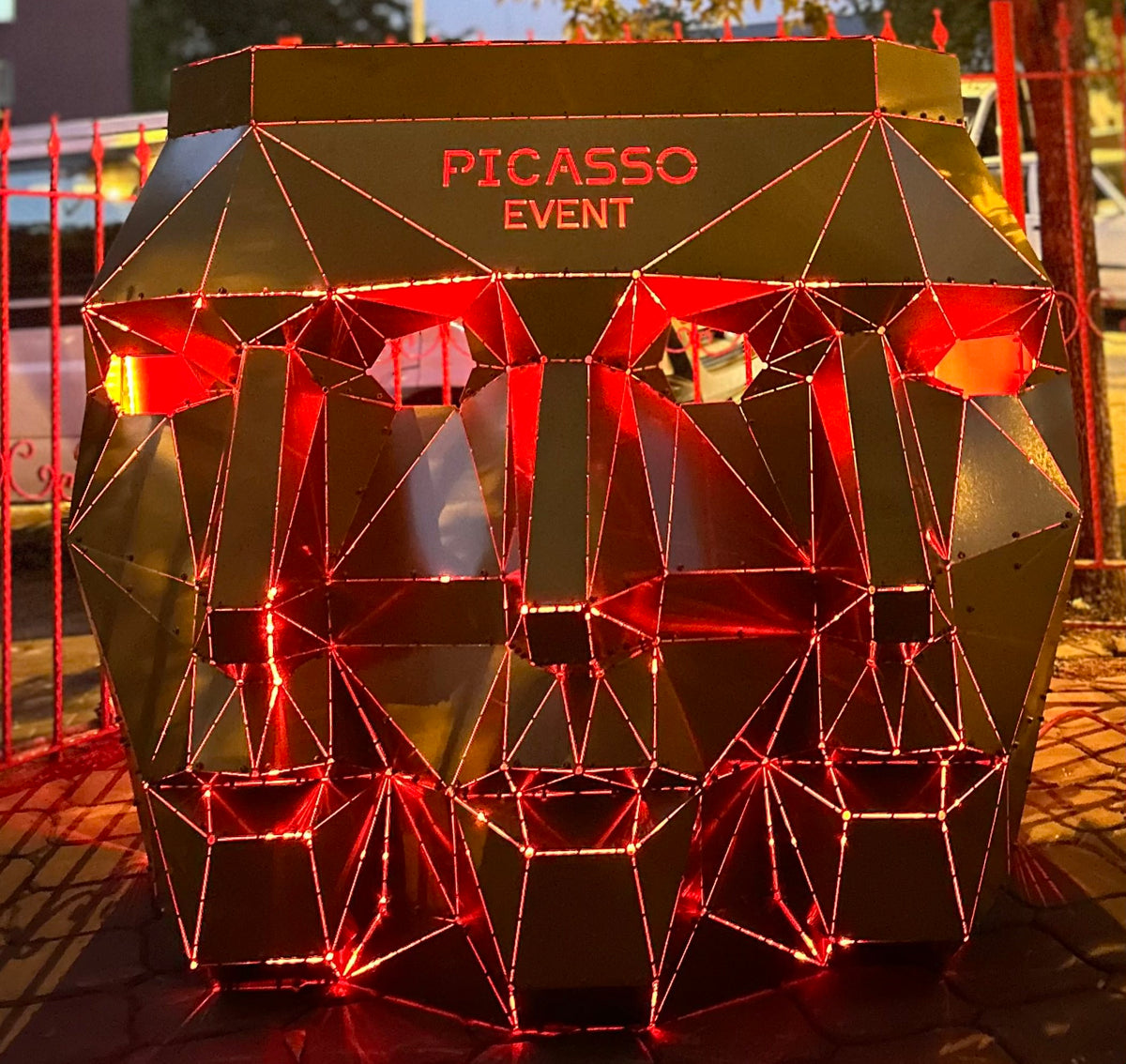 Low-poly metal face sculpture with red neon lighting and 'PICASSO EVENT' text