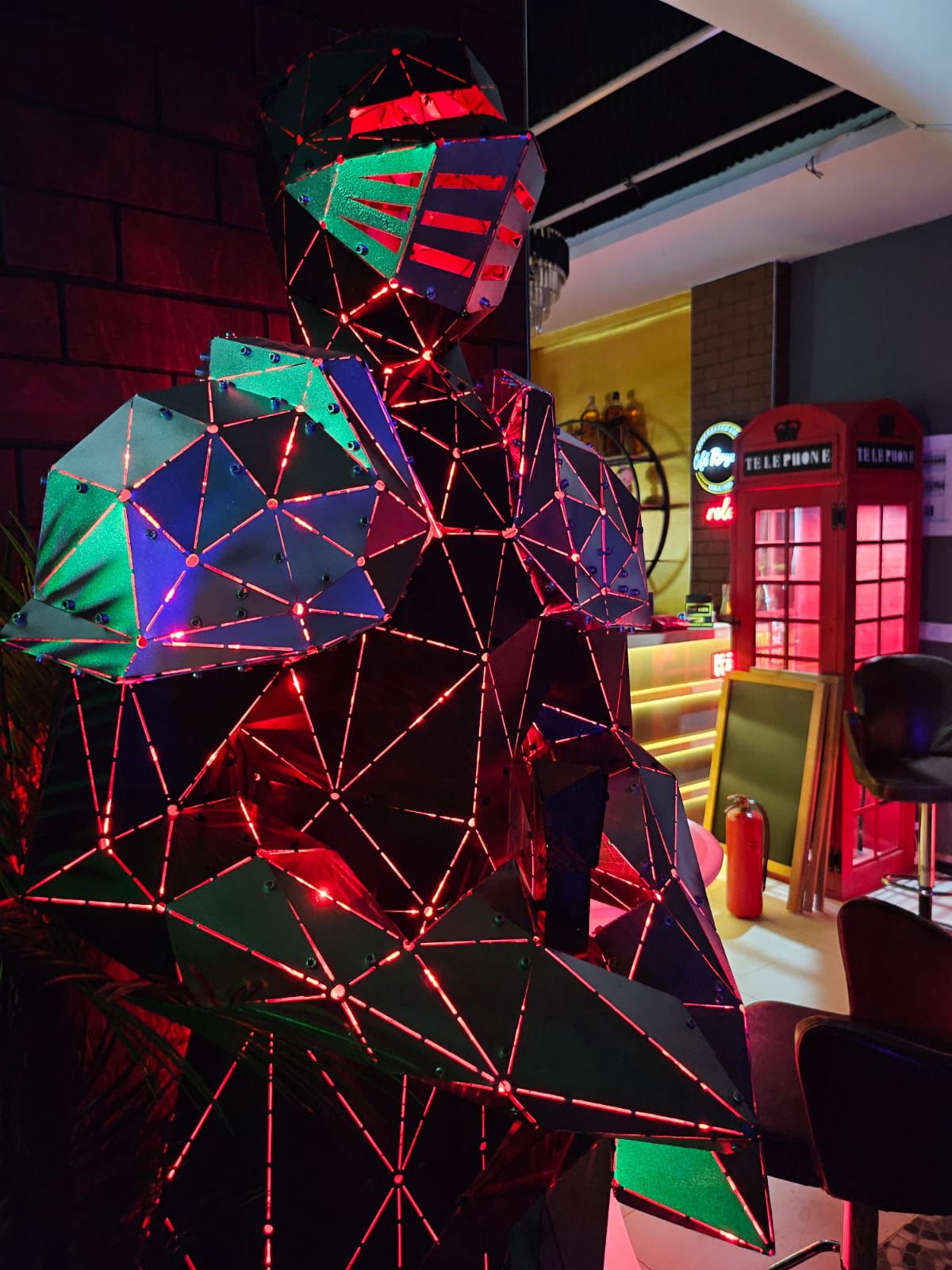 Low-poly metal humanoid sculpture with red glowing edges in a modern interior