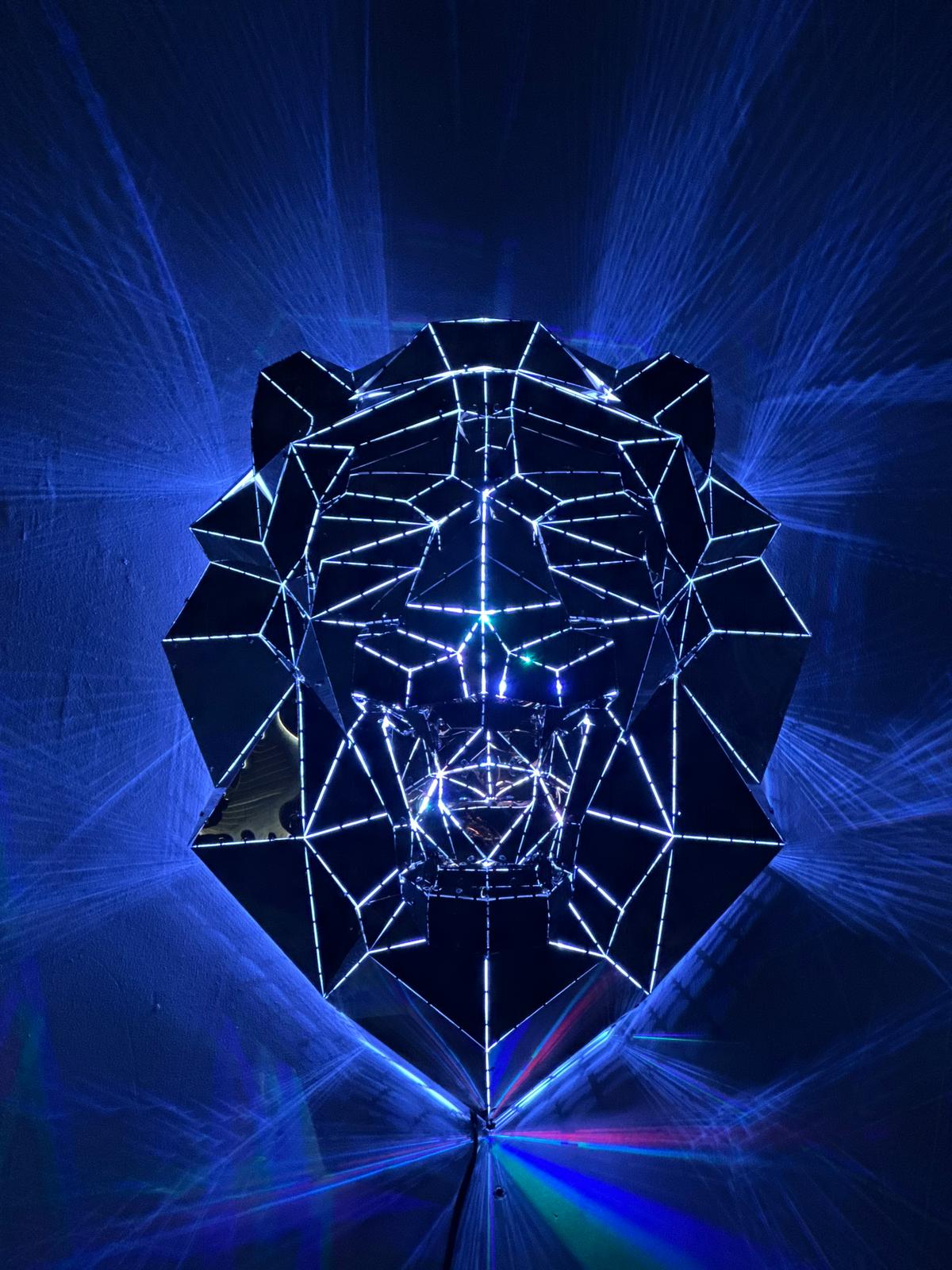 Low-poly metal lion head sculpture illuminated by blue laser light rays