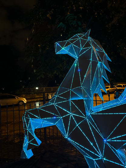 Low-poly metal Pegasus winged horse sculpture with blue LED lighting at night