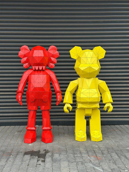 Two geometric low-poly metal sculptures of a red and yellow bear figure against a grey wall.