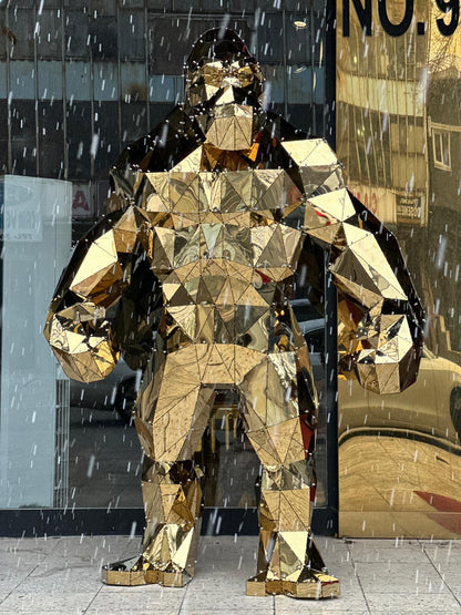 Luxury geometric gold metal gorilla sculpture standing in a storefront during snowfall.