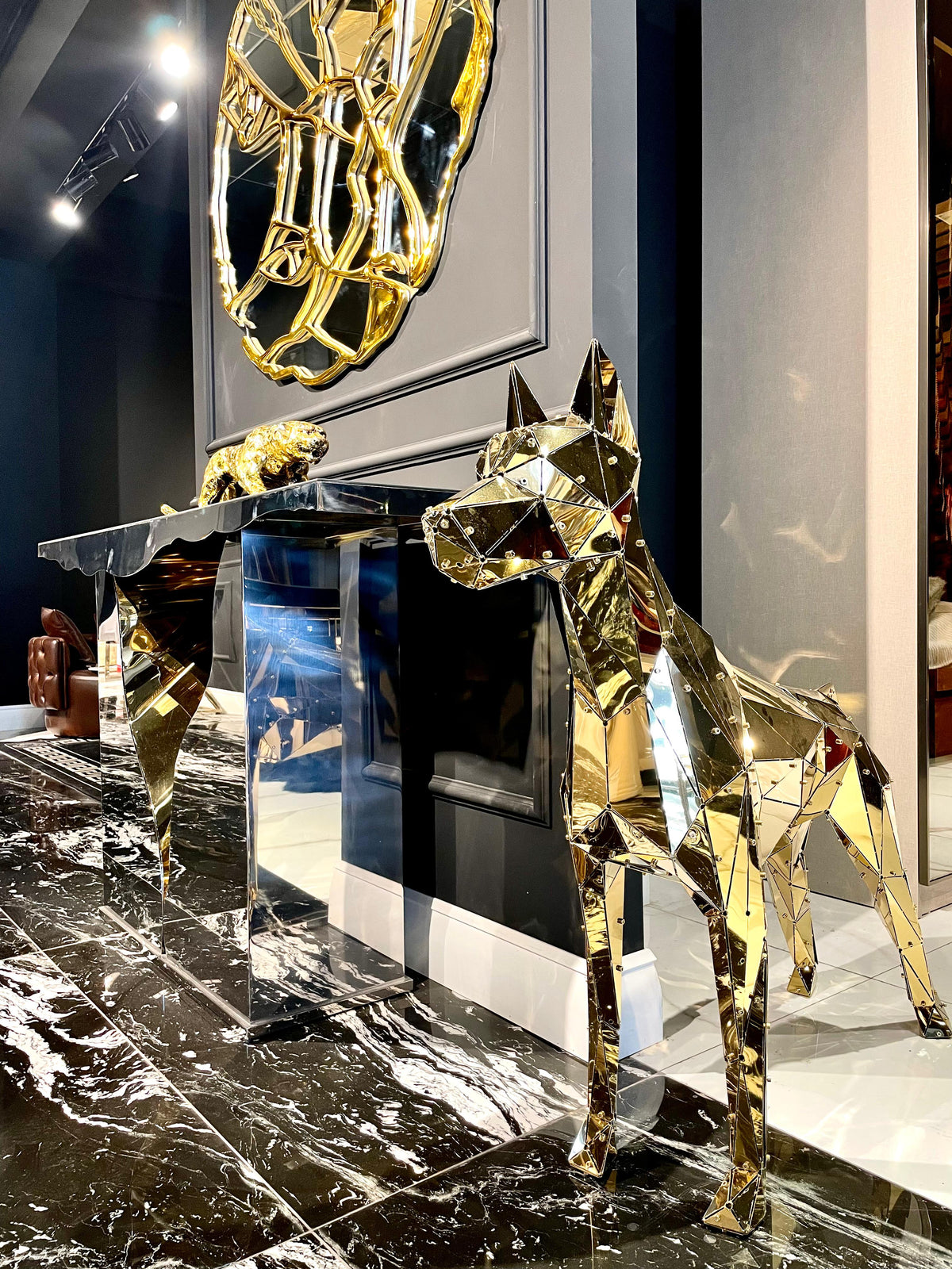Luxury gold geometric dog sculpture next to a mirrored console table on marble flooring.