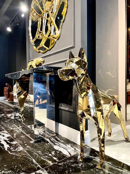 Luxury gold geometric dog sculpture next to a mirrored console table on marble flooring.