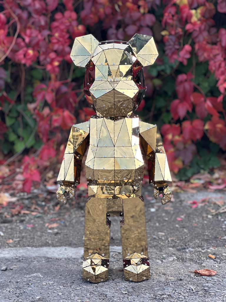 Luxury gold mirrored geometric bear sculpture standing against red autumn foliage