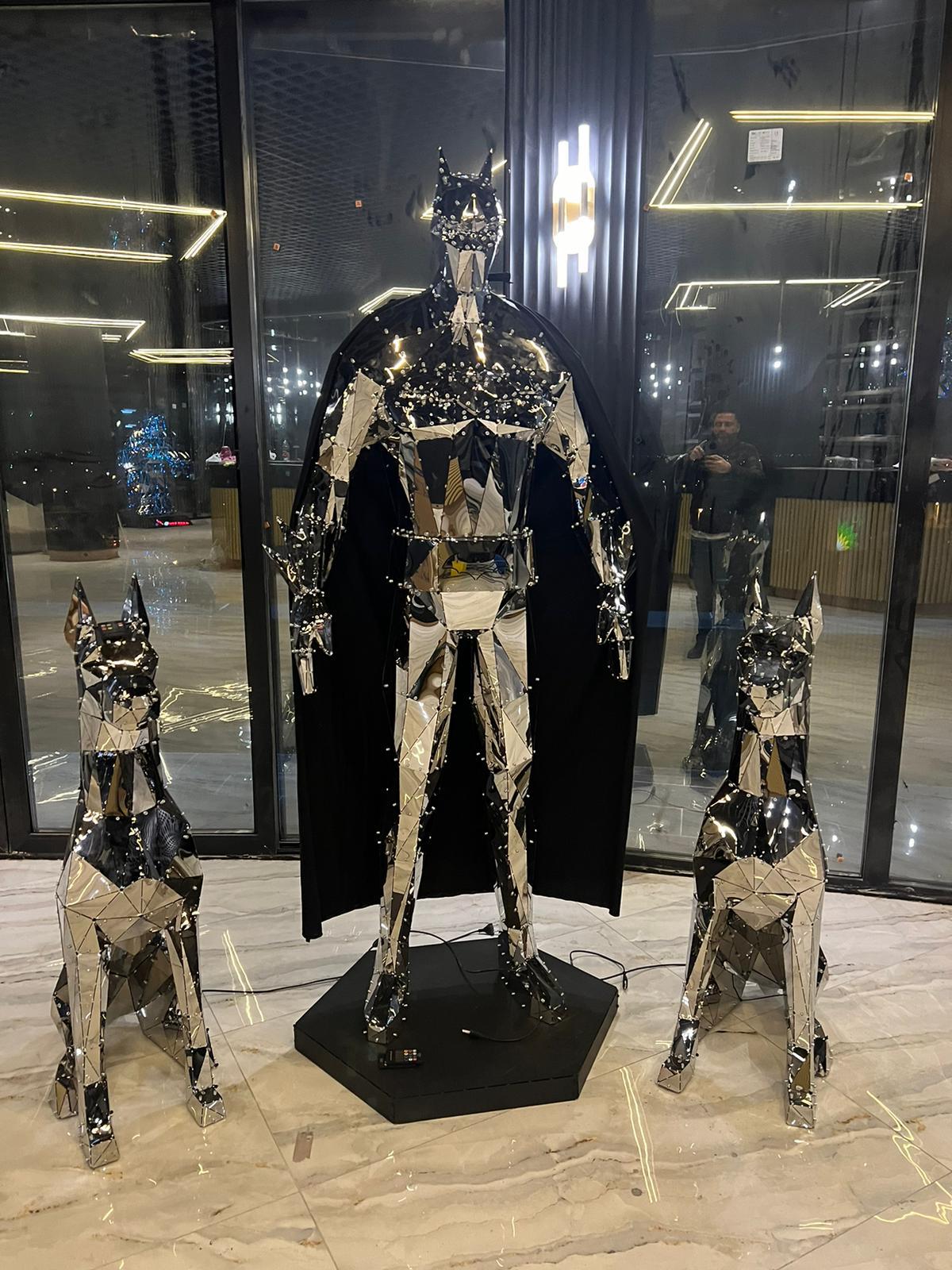 Luxury polished metal low-poly caped hero sculpture flanked by two matching Doberman statues