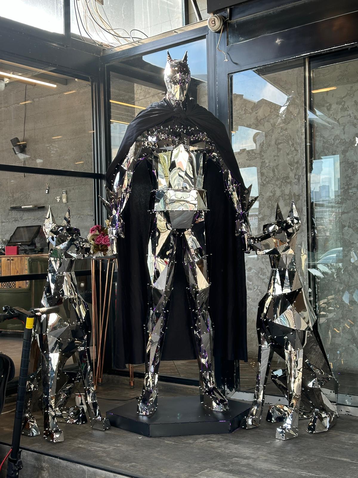 Luxury handcrafted polished metal sculpture of a masked hero in a cape with two metal dogs.