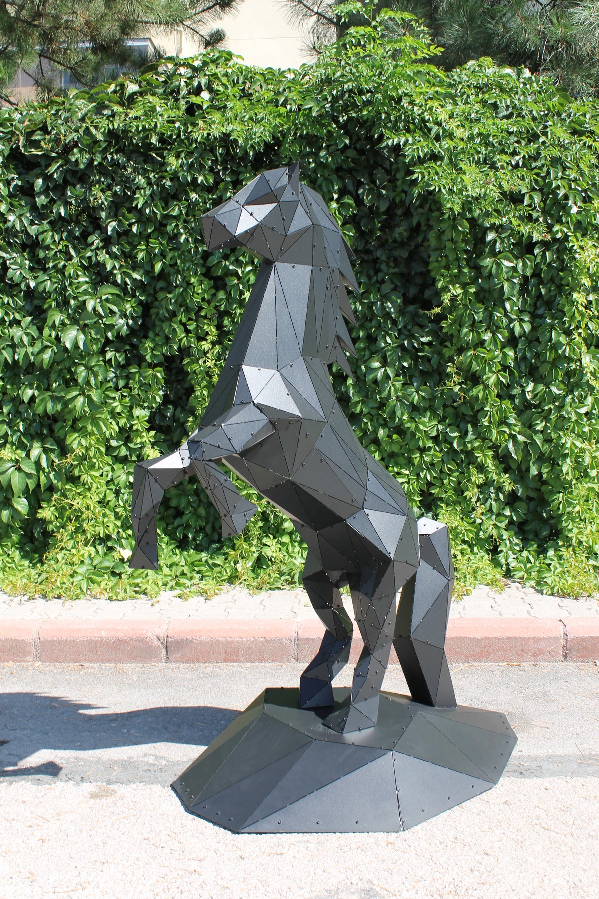 Modern geometric metal sculpture of a rearing horse in matte black against green foliage