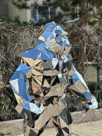 Mirror-polished geometric stainless steel gorilla sculpture in an outdoor garden setting