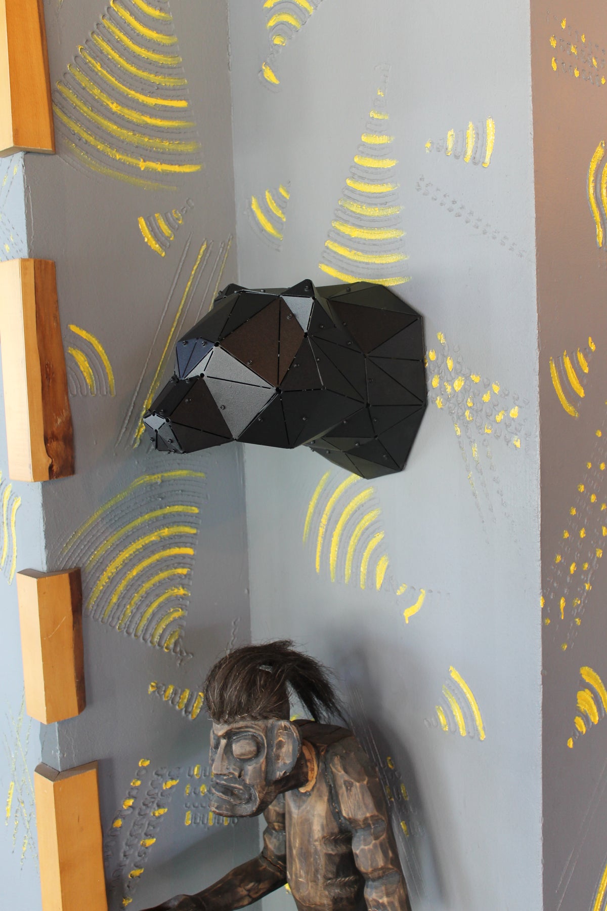 Modern black geometric bear head wall sculpture mounted on a gray wall with yellow art