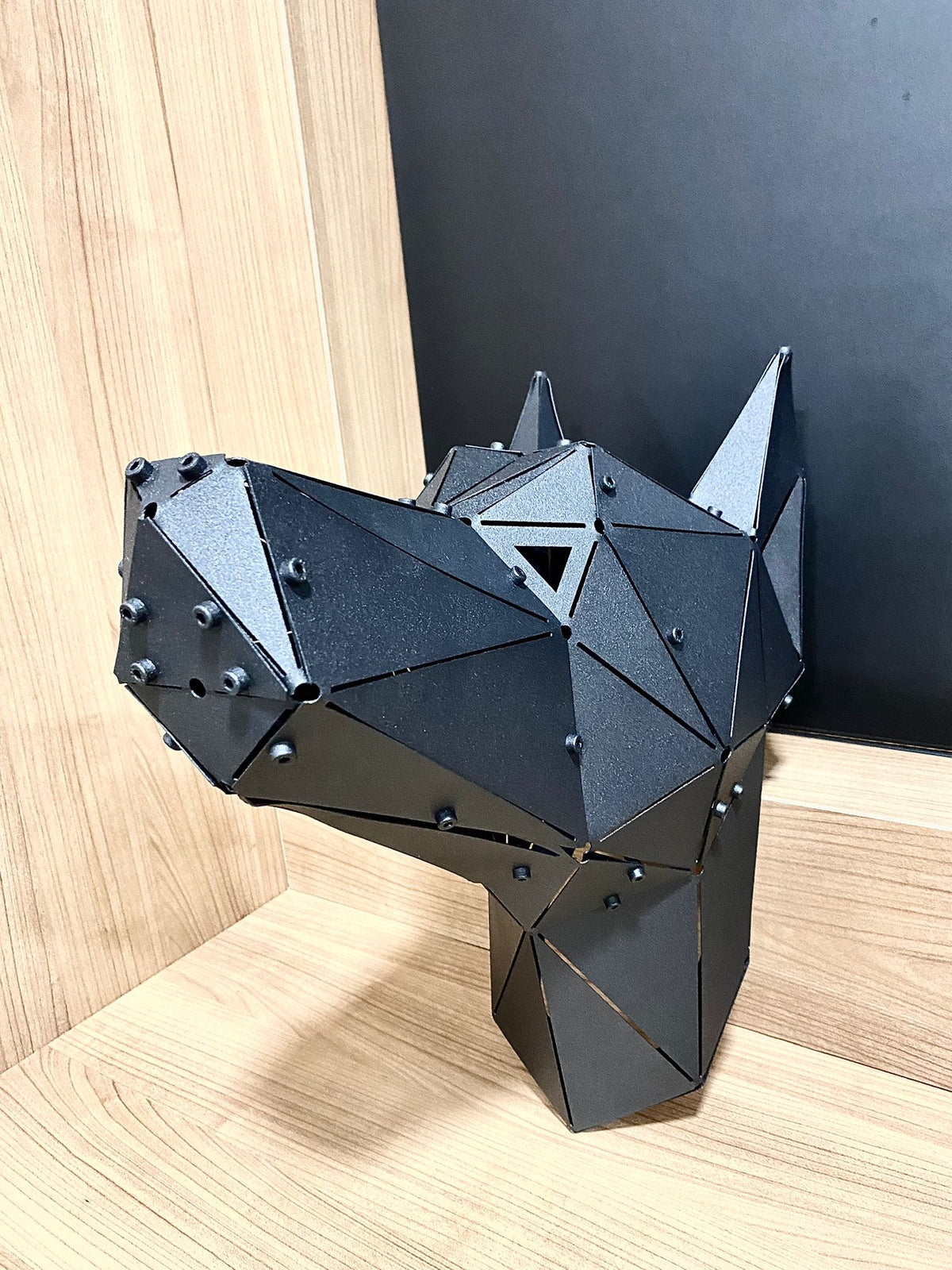 Modern black geometric metal animal head sculpture on a light wood surface