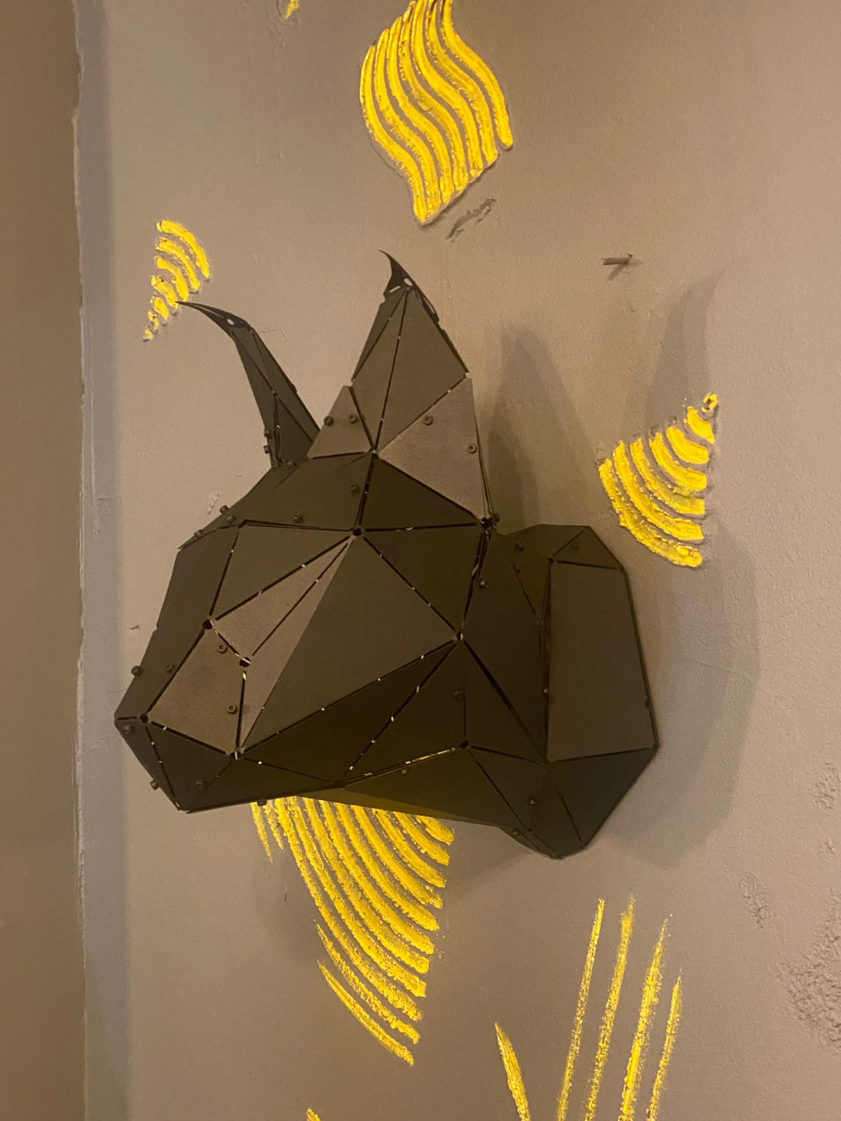 Modern geometric black metal lynx head sculpture on a gray wall with yellow art