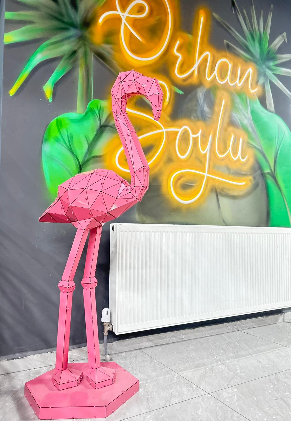 Modern geometric pink metal flamingo sculpture against a colorful tropical wall backdrop