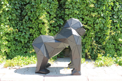 Modern low-poly black metal gorilla sculpture in side view against a lush green hedge backdrop