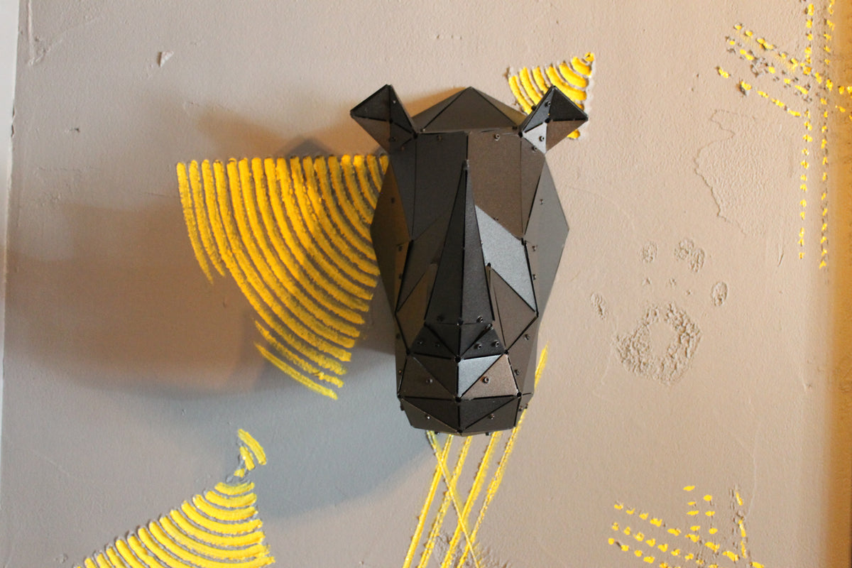Modern low-poly black metal rhinoceros head sculpture mounted on a grey wall with yellow art.