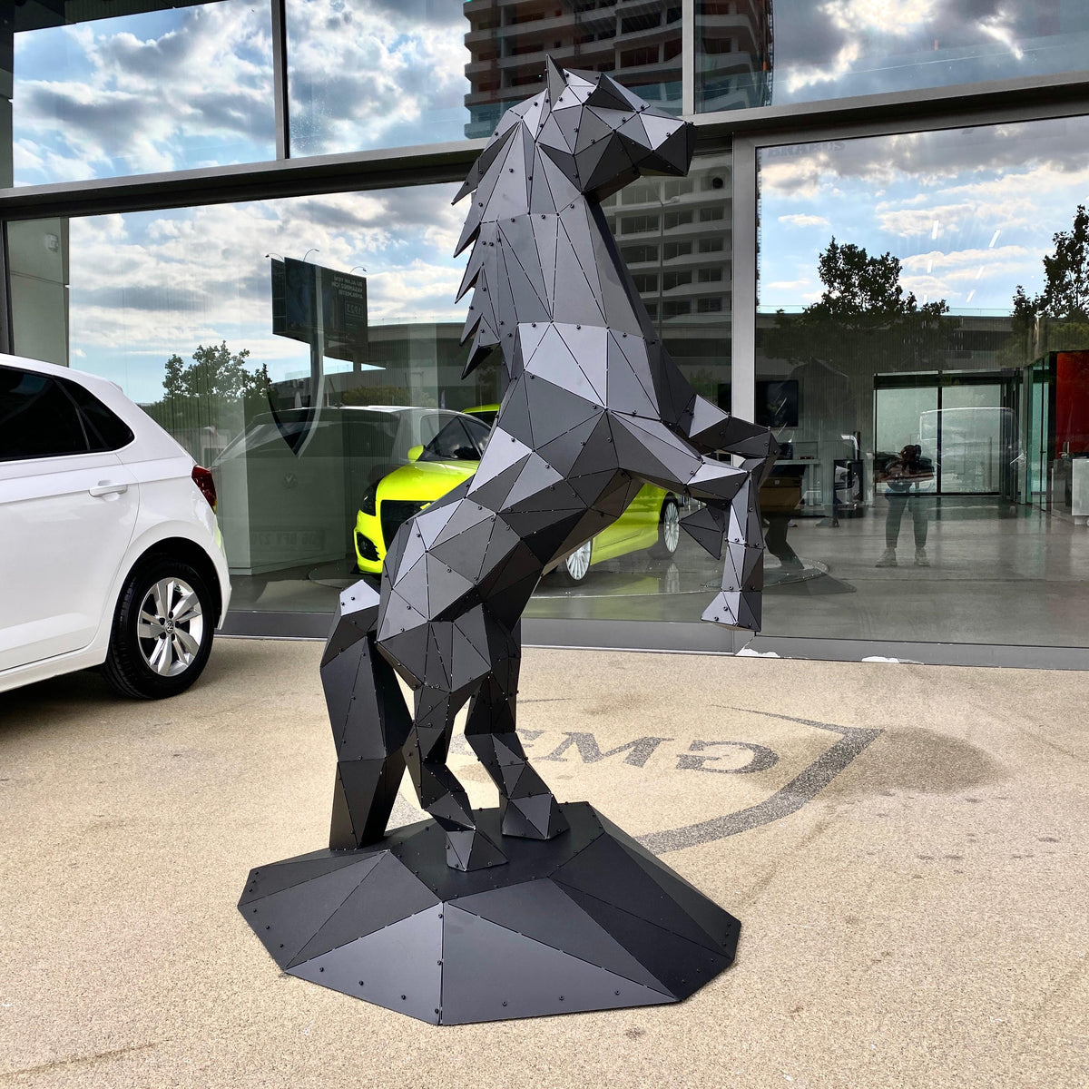 Modern low-poly metal horse sculpture rearing up on a concrete surface outdoors.