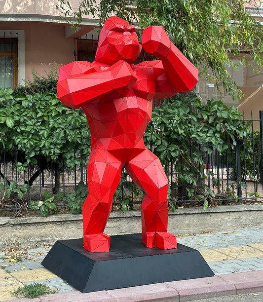 Modern low-poly red metal gorilla sculpture on a black base outdoors