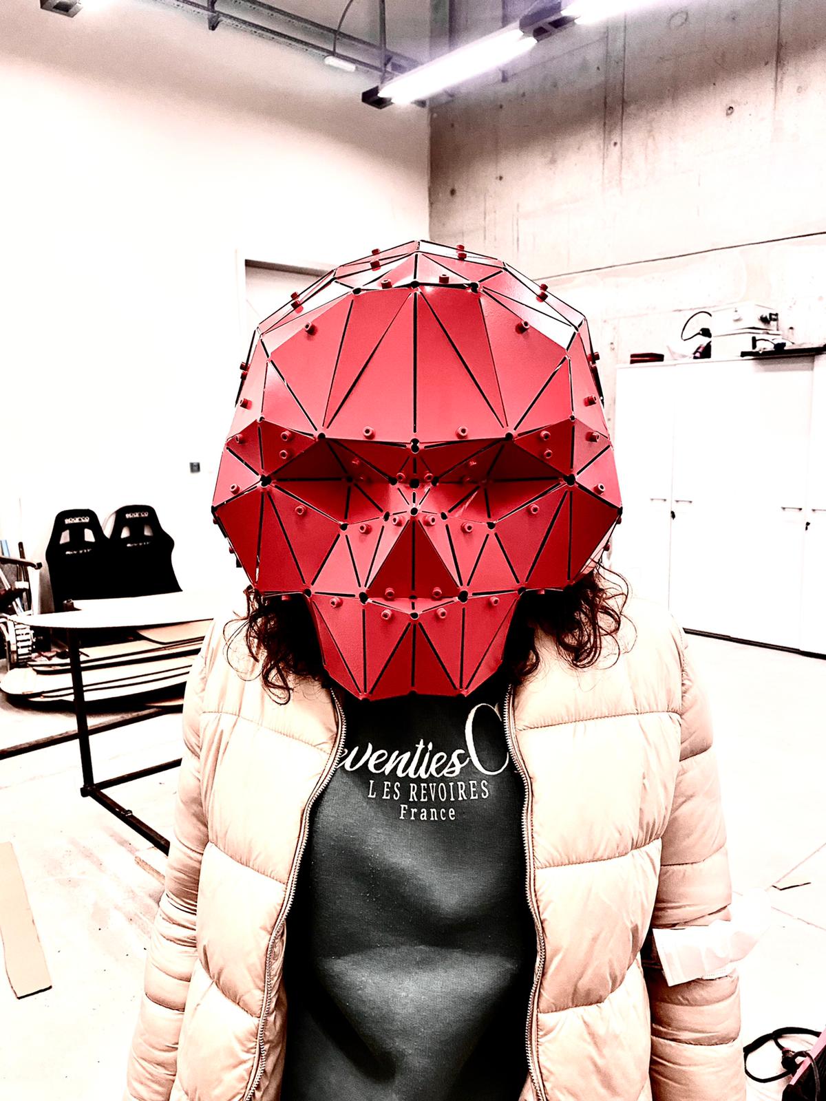 Person wearing a red geometric low-poly metal skull mask handcrafted by Metart Atelier.