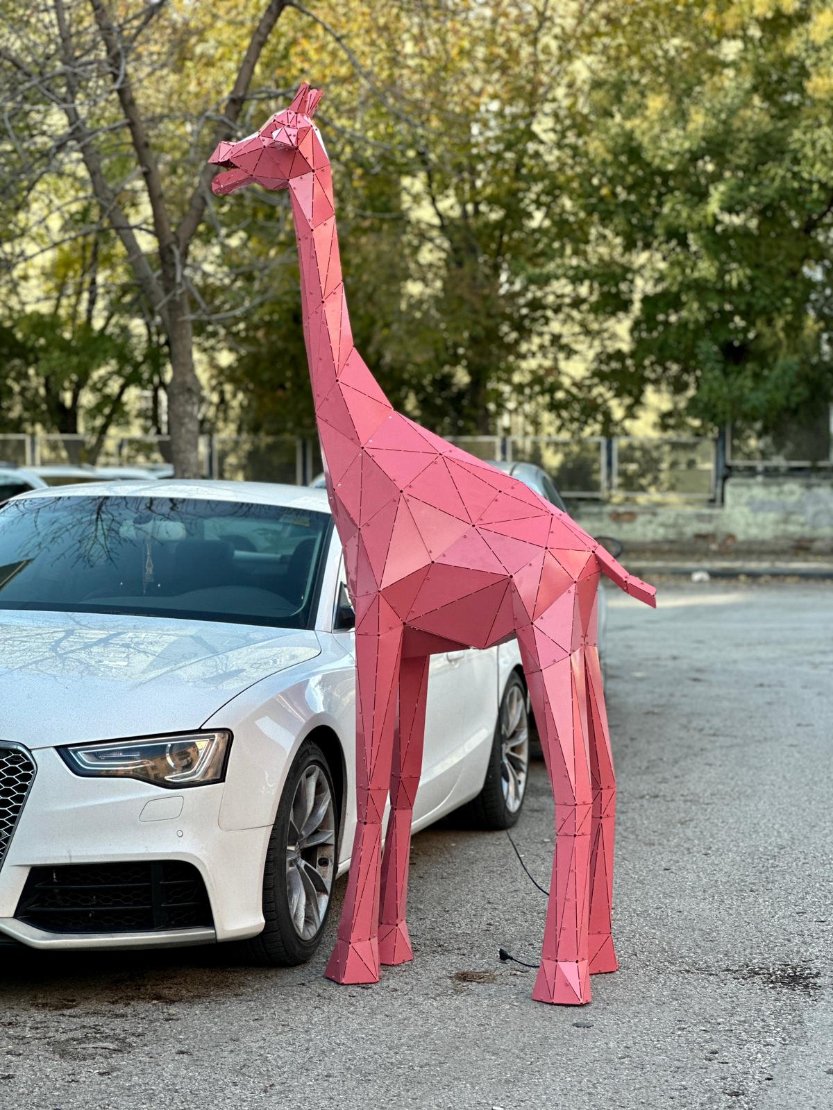 Pink geometric metal giraffe sculpture standing next to a white car