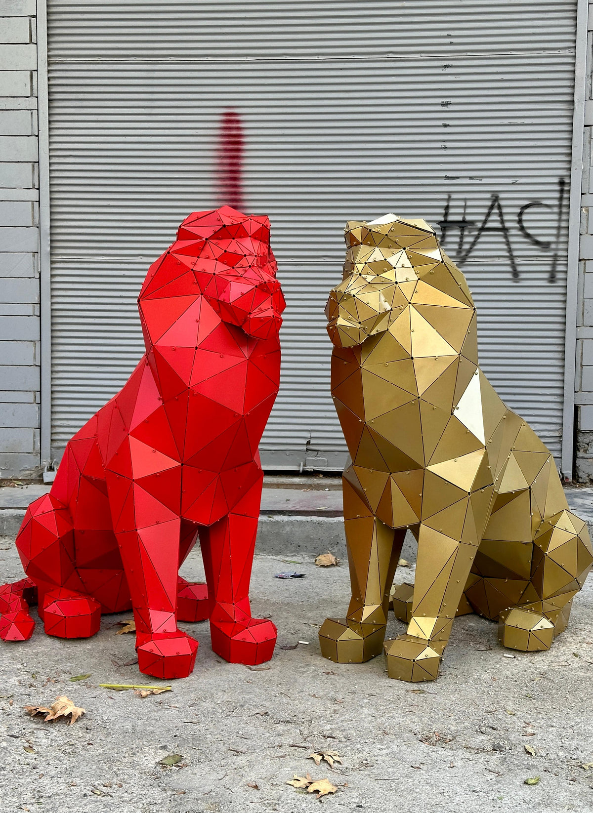 Two geometric metal lion sculptures, one red and one gold, against a grey shutter background.
