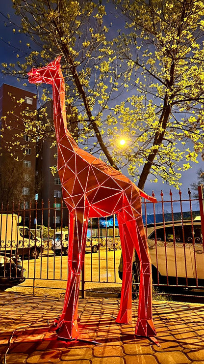 Red geometric metal giraffe sculpture illuminated at night in an urban setting