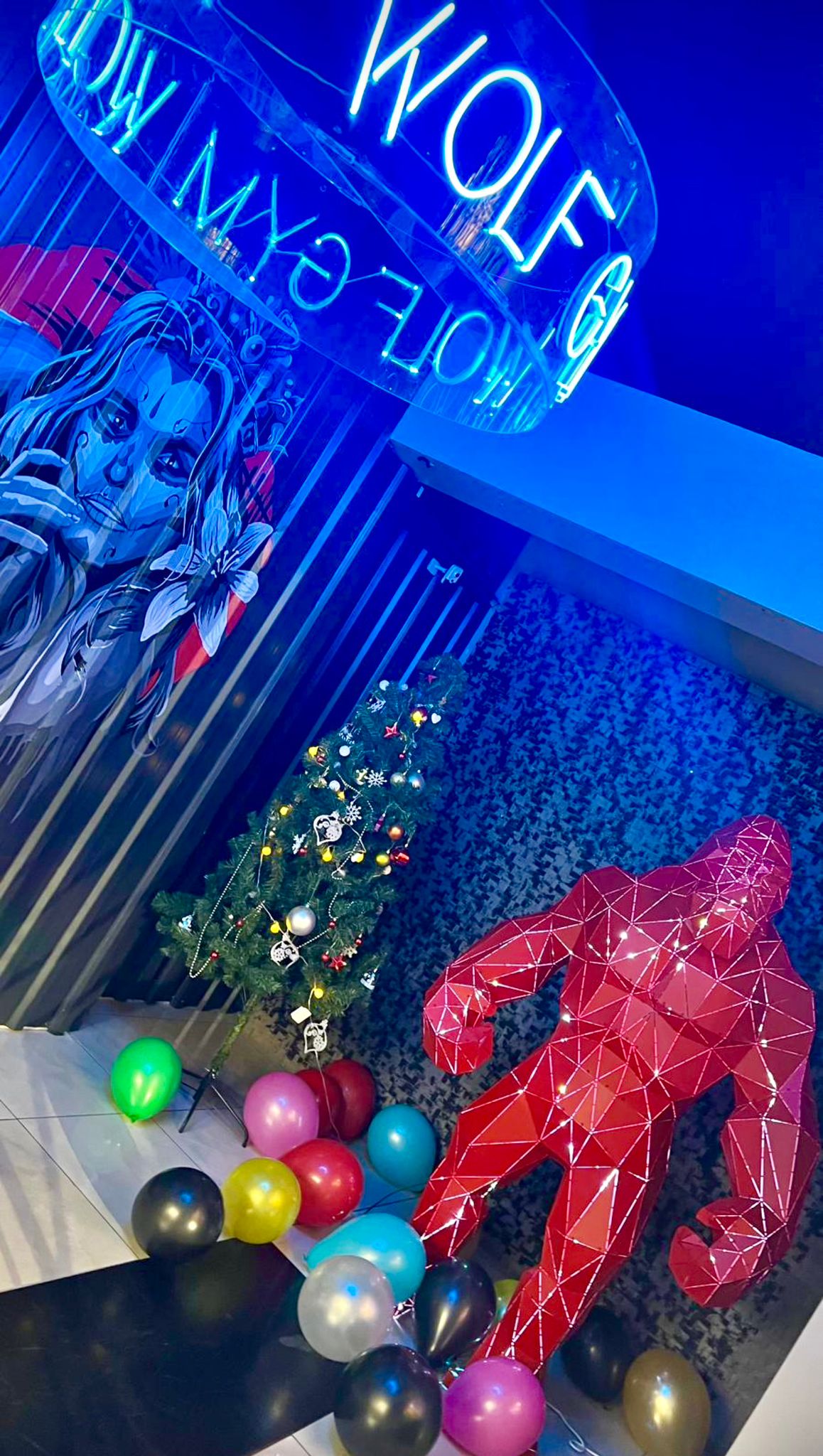 Red geometric gorilla metal sculpture with balloons and a Christmas tree in a neon-lit studio