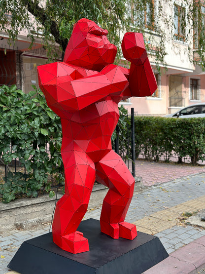 Red geometric metal gorilla sculpture standing on a black base outdoors