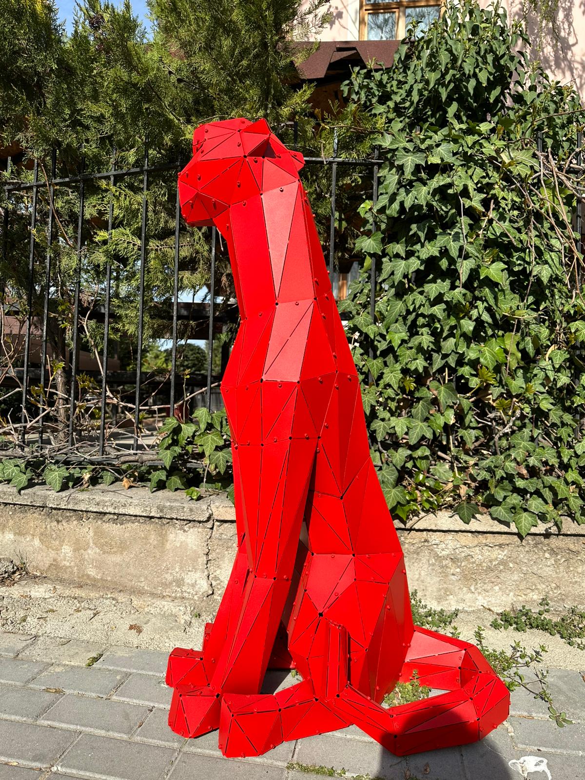 Red geometric metal sculpture of a sitting leopard in an outdoor garden setting