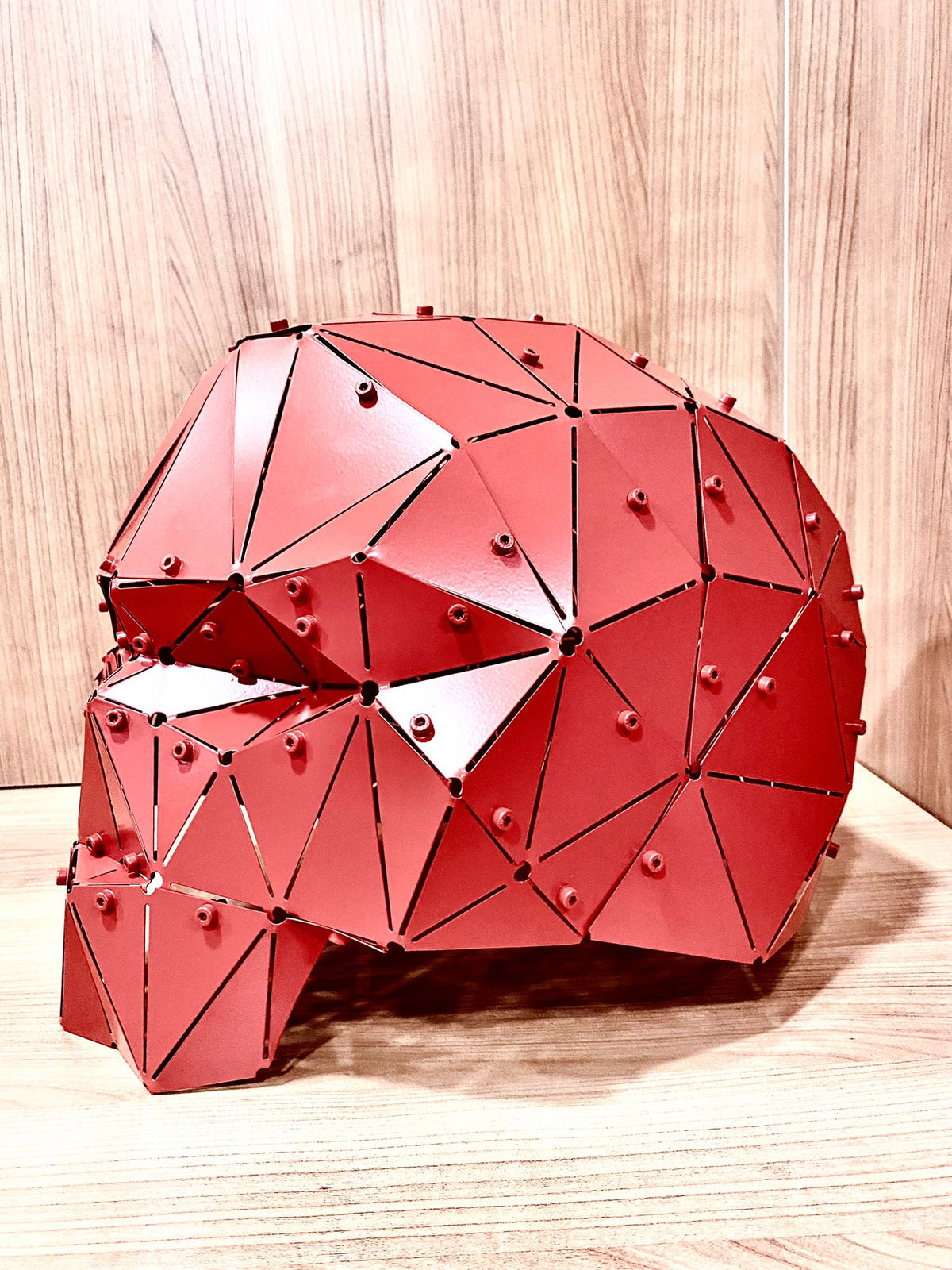 Red low-poly geometric metal skull sculpture on a wooden surface