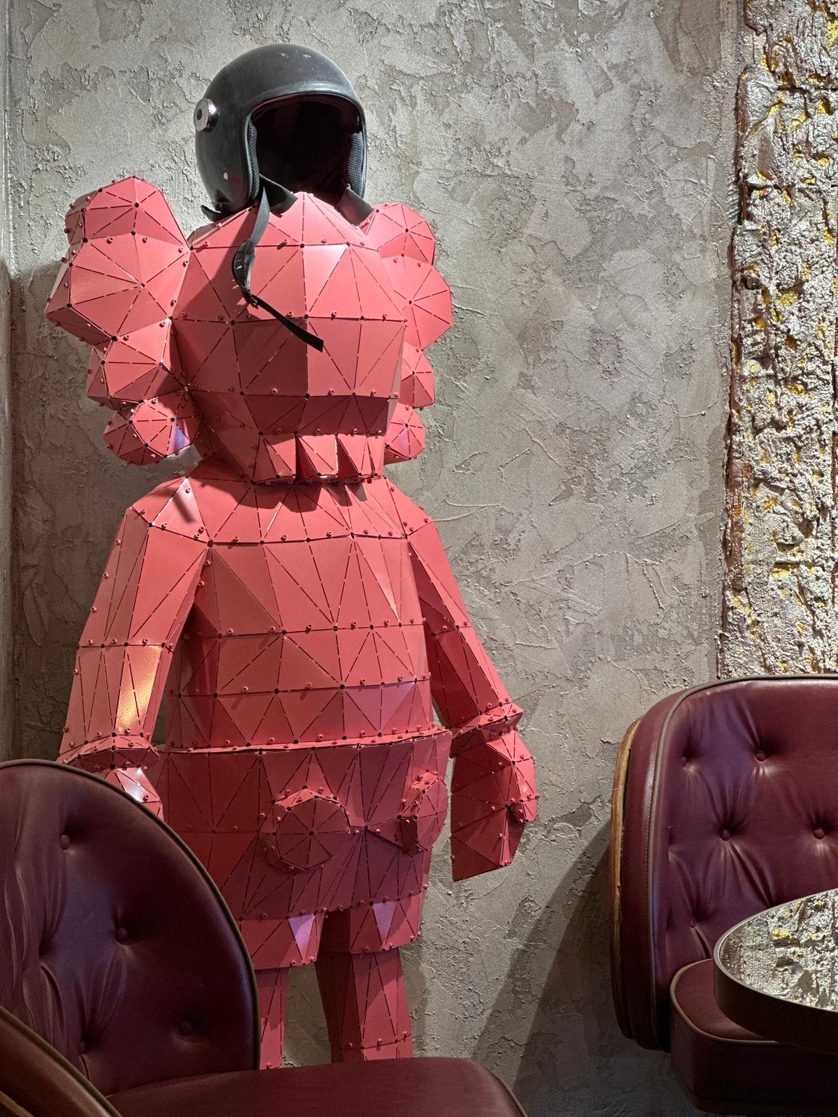 Red low-poly metal sculpture of a figure wearing a black motorcycle helmet