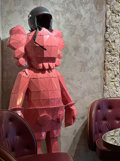 Red low-poly metal sculpture of a figure wearing a black motorcycle helmet