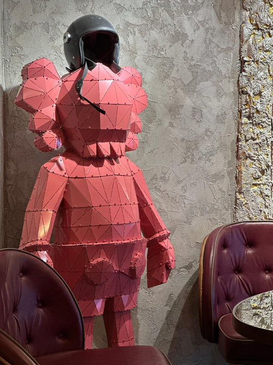 Red low-poly metal sculpture of a figure wearing a black motorcycle helmet
