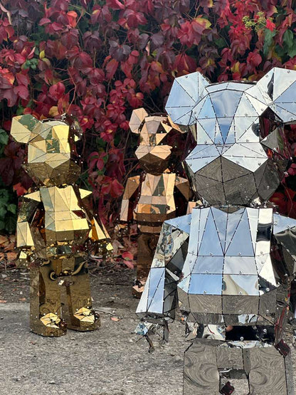 Three geometric metal bear sculptures in gold, bronze, and silver finishes against red foliage.