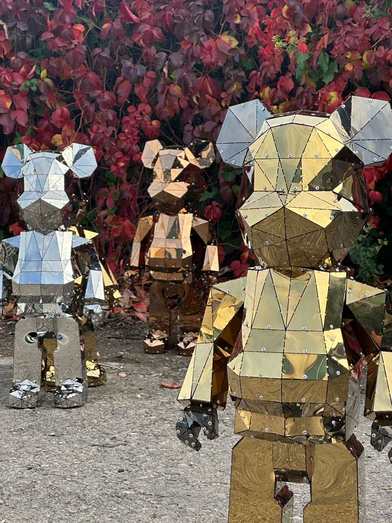 Three mirrored geometric bear sculptures in silver and gold tones against red autumn leaves.