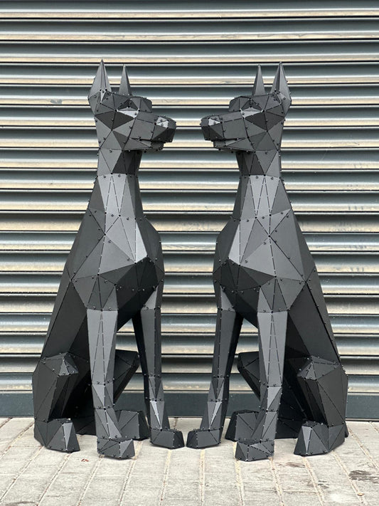 Two black geometric metal dog sculptures facing each other against a ribbed grey wall.