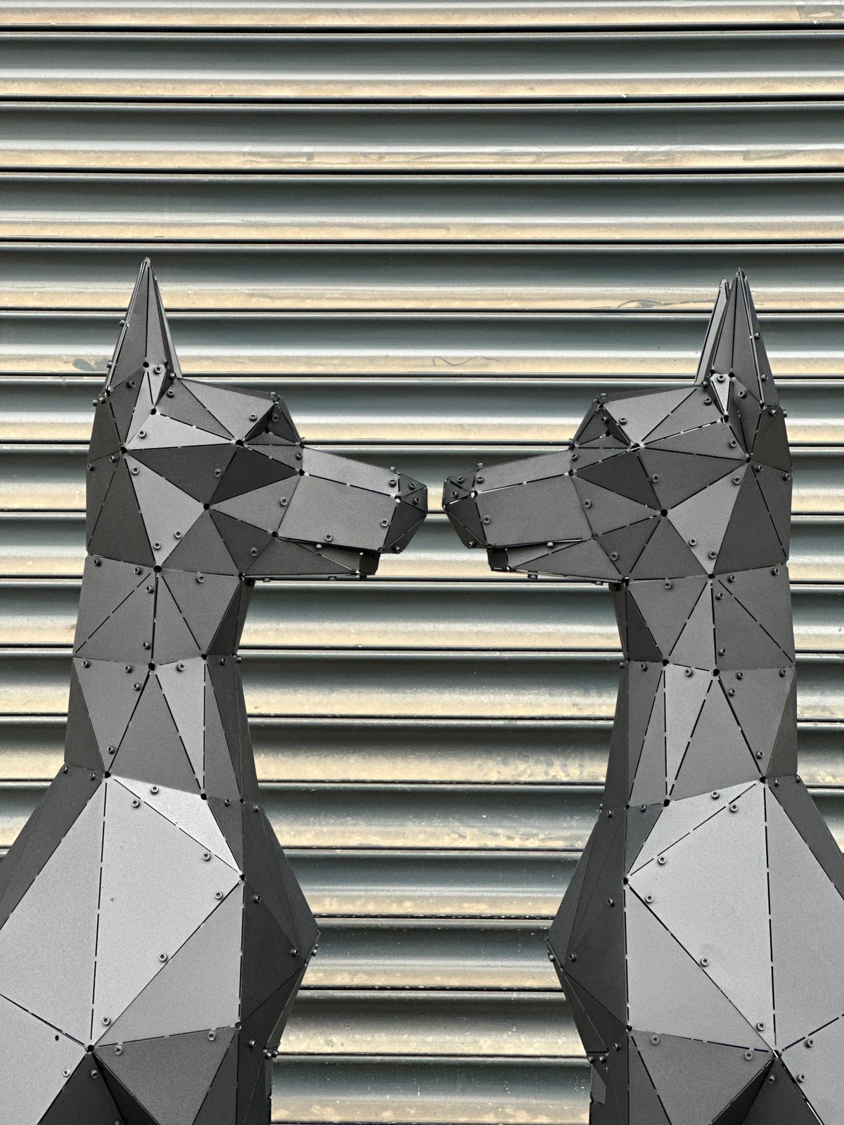 Two geometric black metal dog sculptures facing each other against a ribbed wall.